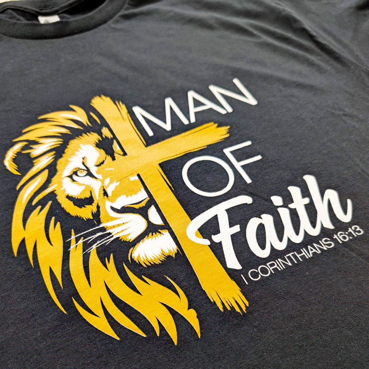 Black t-shirt with yellow lion graphic and cross, featuring 'Man of Faith' text.