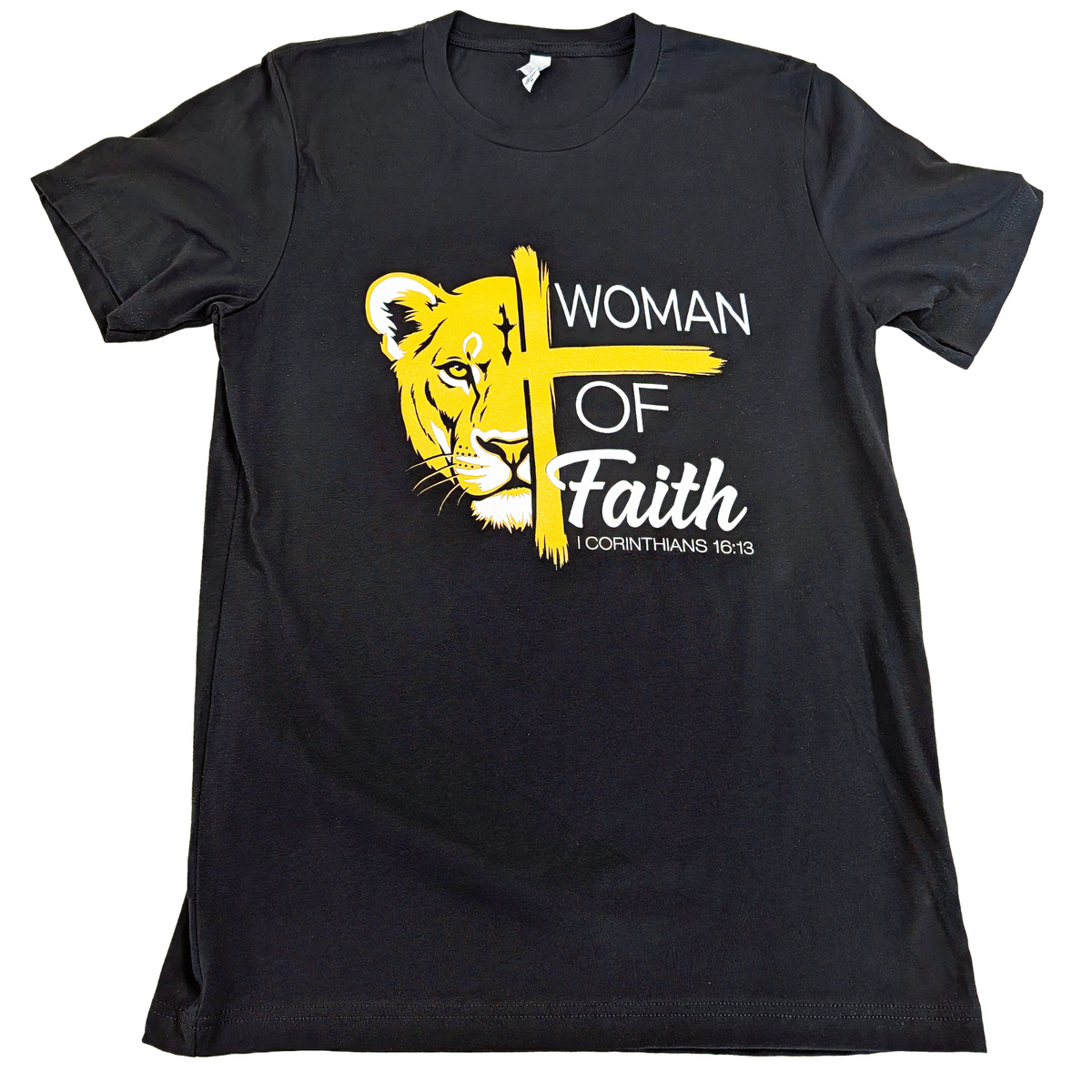 Black t-shirt with yellow lion graphic and cross, featuring text 'Woman of Faith 1 Corinthians 16:13' on a white background.